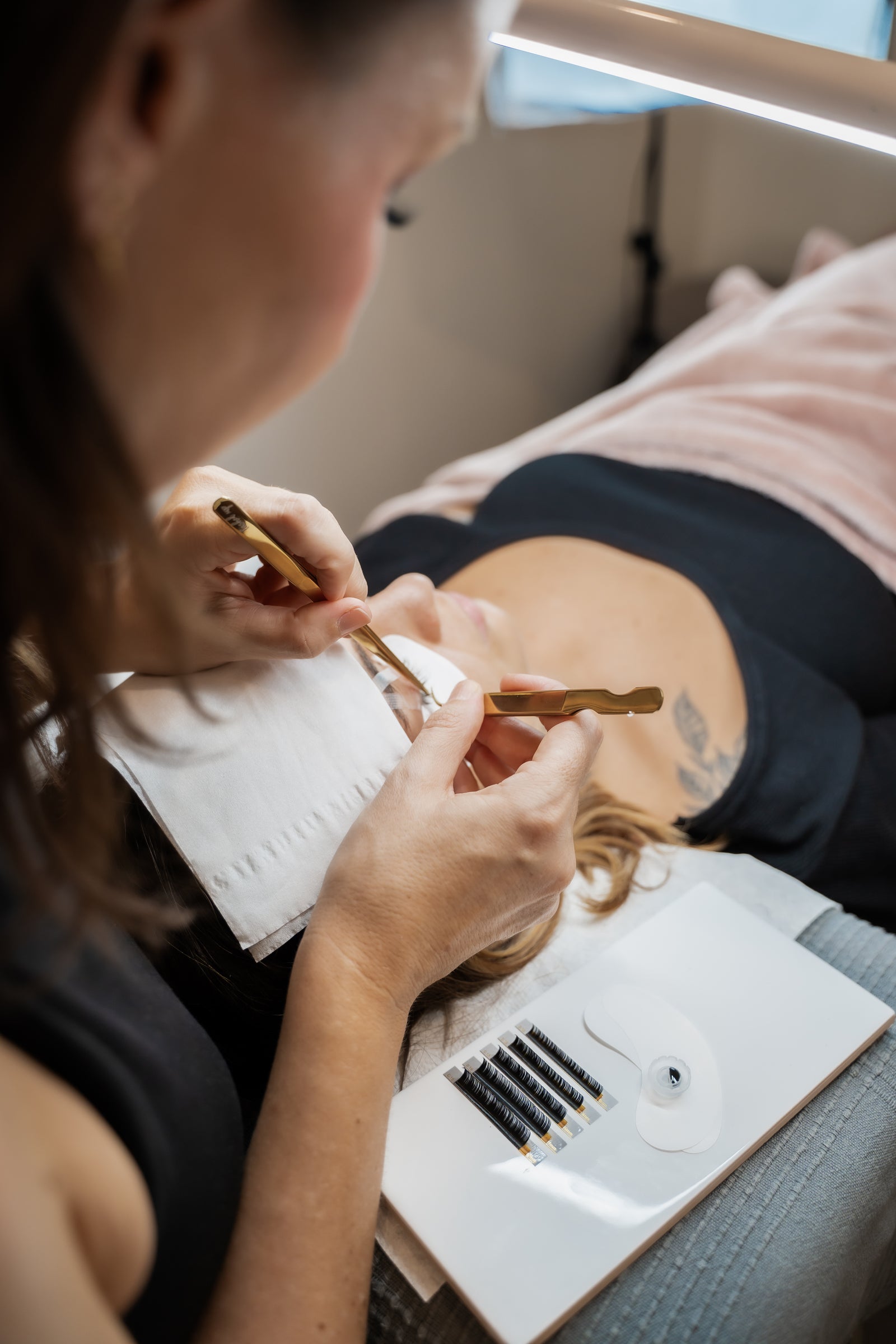 Lash educator applying lash extensions with gold tweezers